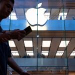 A pedestrian uses a smartphone while walking past an Apple store and logo in Hong Kong.