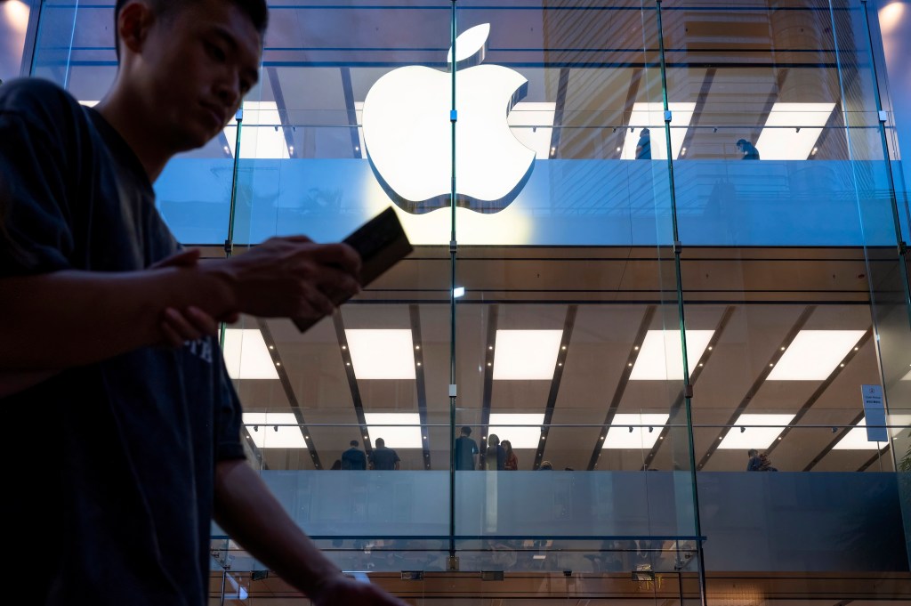 A pedestrian uses a smartphone while walking past an Apple store and logo in Hong Kong.