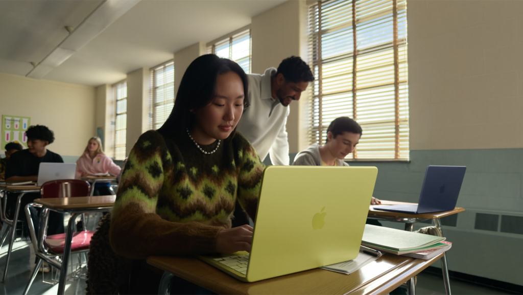 young woman seated at a classroom desk using a MacBook Neo