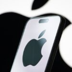 In this photo illustration, the logo of Apple Inc. is displayed on a smartphone screen, with the company's iconic black apple symbol visible in the background.