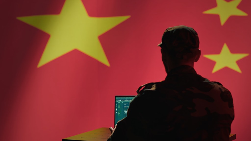 A man sits in front of a computer and the Chinese flag.