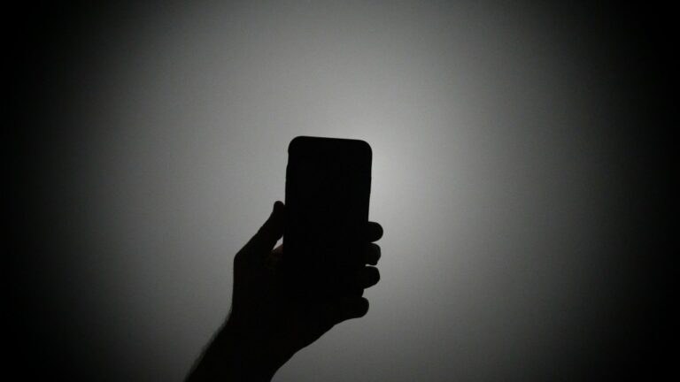 The silhouette of a hand holding an iPhone with the light on.