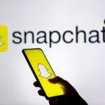 In this photo illustration, a woman's silhouette holds a smartphone with the Snapchat logo displayed on the screen and in the background.