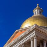 The gold dome of the Massachusetts State House stands against a blue sky.