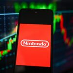 Nintendo logo is seen displayed on a smartphone with stock market percentages on the background.