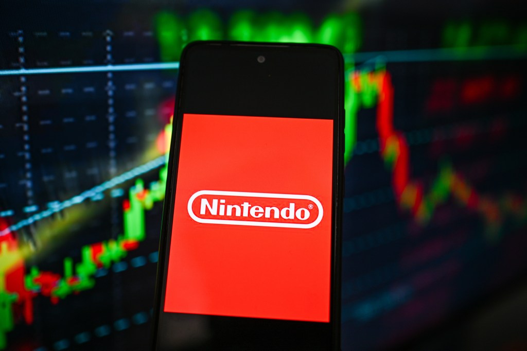 Nintendo logo is seen displayed on a smartphone with stock market percentages on the background.