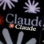 The Claude logo is displayed on a smartphone screen placed on a reflective surface onto which a multitude of Claude logos are projected.