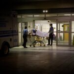 a person wheeled in on an ambulance stretcher outside of a U.S. emergency room at night