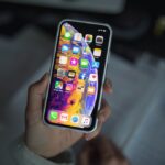 a person holding new iPhone XS smartphone in their hand over a notepad.
