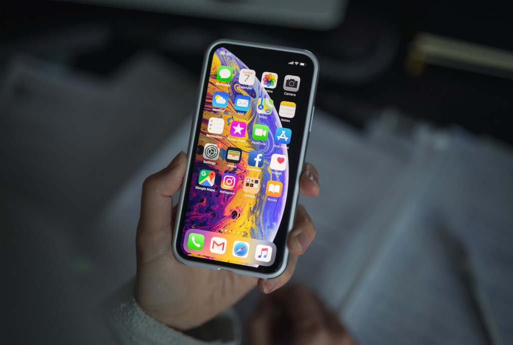 a person holding new iPhone XS smartphone in their hand over a notepad.