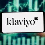 The logo of US marketing automation company Klaviyo Inc. is seen displayed on a smartphone in front of an abstract background on a computer screen.