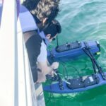 Members of the University of Florida team release an autonomous vessel for testing its magnetoelectric antennas for underwater communication with a submerged drone below.