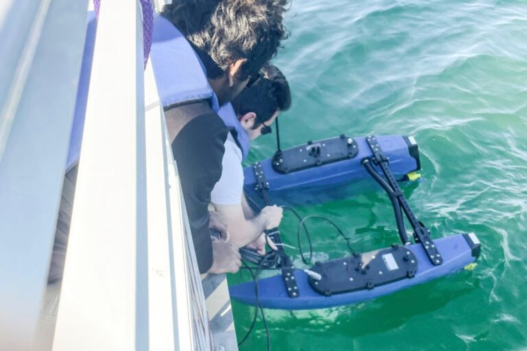Members of the University of Florida team release an autonomous vessel for testing its magnetoelectric antennas for underwater communication with a submerged drone below.