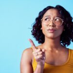 Confused woman, thinking bubble and studio mockup background. Pensive, annoyed or curious person contemplating decision. Girl with solution or idea pointing for marketing advertisement.