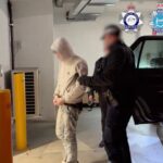 a photo of australian police walking with one of the alleged TeamPCP hackers in handcuffs