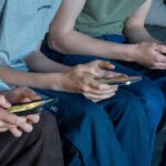 Three teenage boys look at their smartphone screens.
